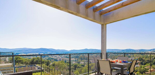 Varanda com mesa e cadeiras, com vista para uma paisagem montanhosa.