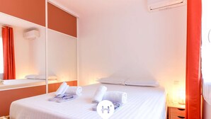 A hotel room with a bed, a wooden nightstand, a mirror, and a window with red curtains. - Stunning 3P in Lavandou center with garden, pets allowed (Le Lavandou)