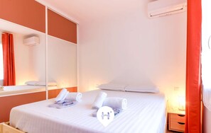 A hotel room with a bed, a wooden nightstand, a mirror, and a window with red curtains. - Stunning 3P in Lavandou center with garden, pets allowed (Le Lavandou)