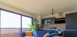 A modern kitchen with a built-in oven, a dining area with a blue sofa, and a large window offering a view.
