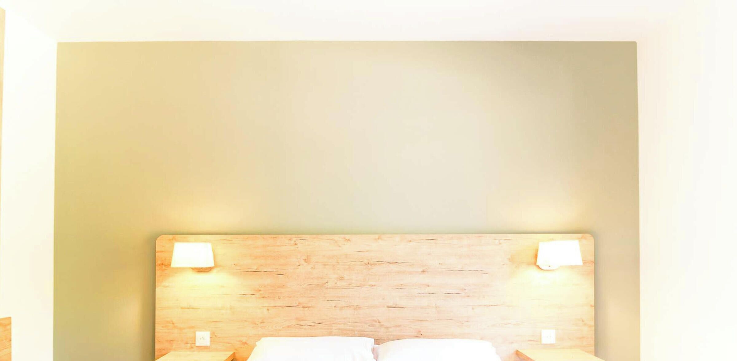 Ein Hotelzimmer mit einem hölzernen Kopfteil, zwei Nachttischlampen und einem Bett mit weißer Bettwäsche.