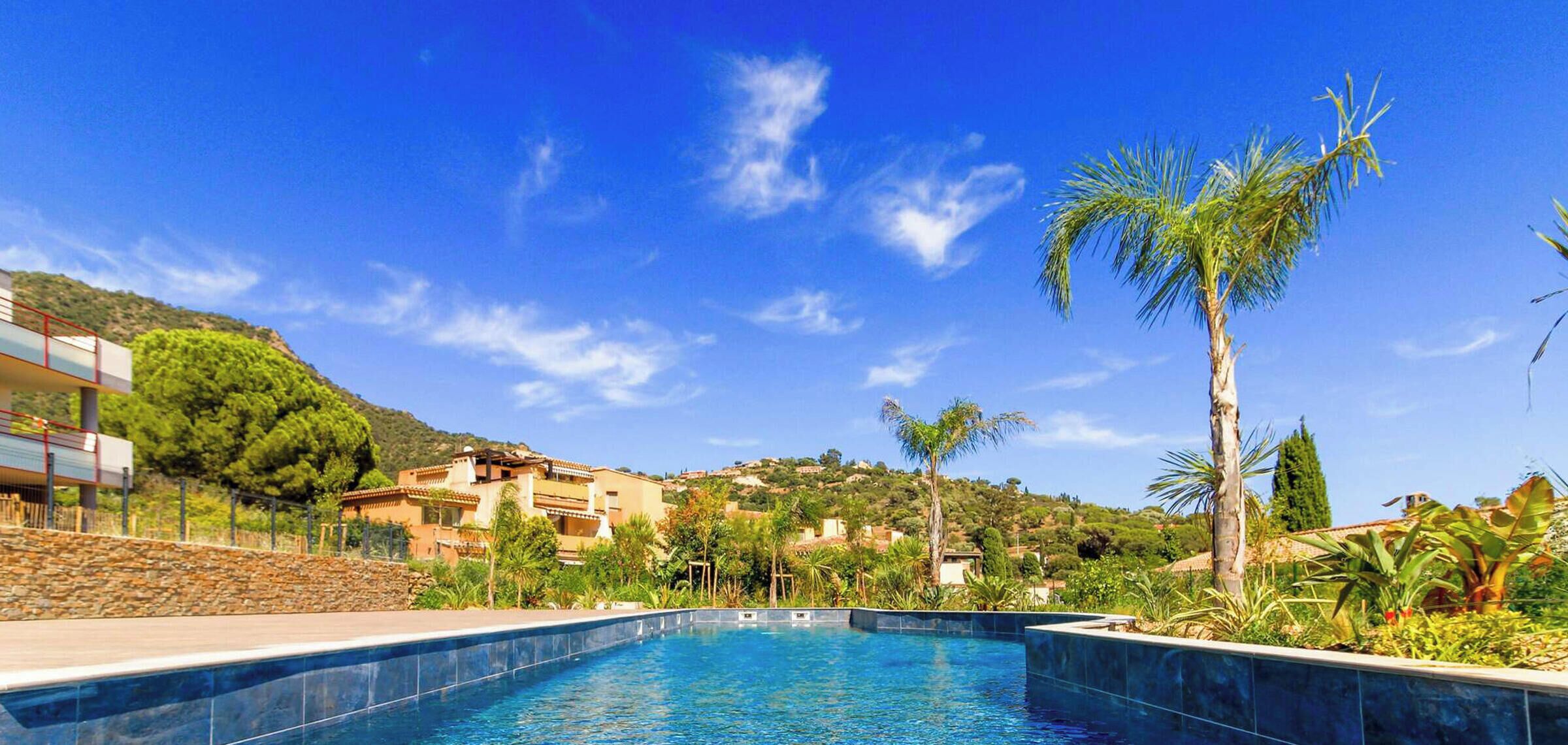 Une piscine bordée d’immeubles et de verdure, avec un ciel bleu dégagé au-dessus.