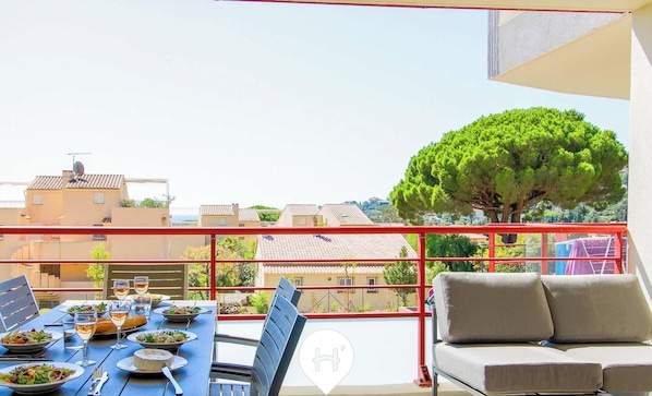 Varanda com mesa para dois, sofá e vista para edifícios e árvores.