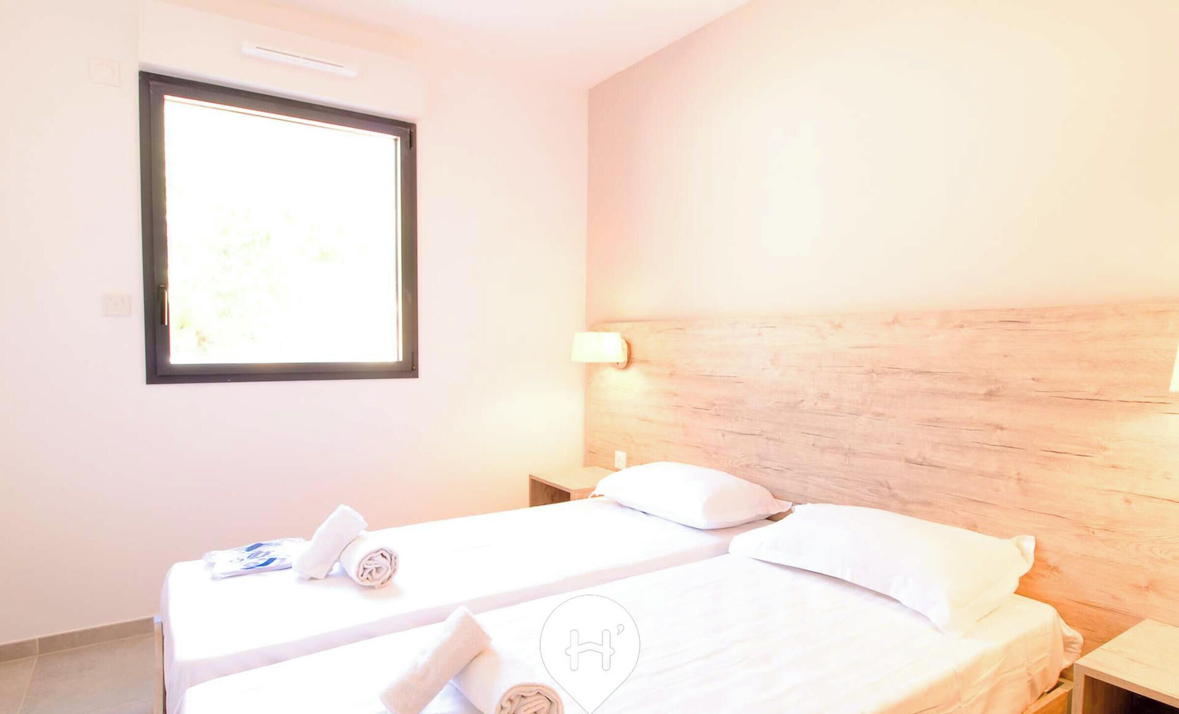 A hotel room with two beds, a window, and a wooden headboard.