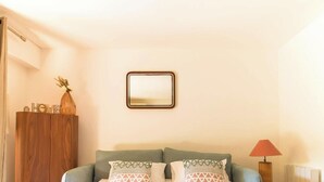 A room with a wooden wardrobe, a green sofa with patterned cushions, a mirror on the wall, and a red lamp.