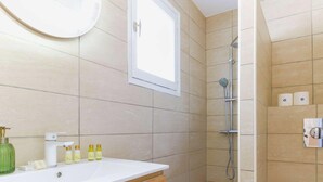 A bathroom with a white sink, toiletries, a shower, and a window.