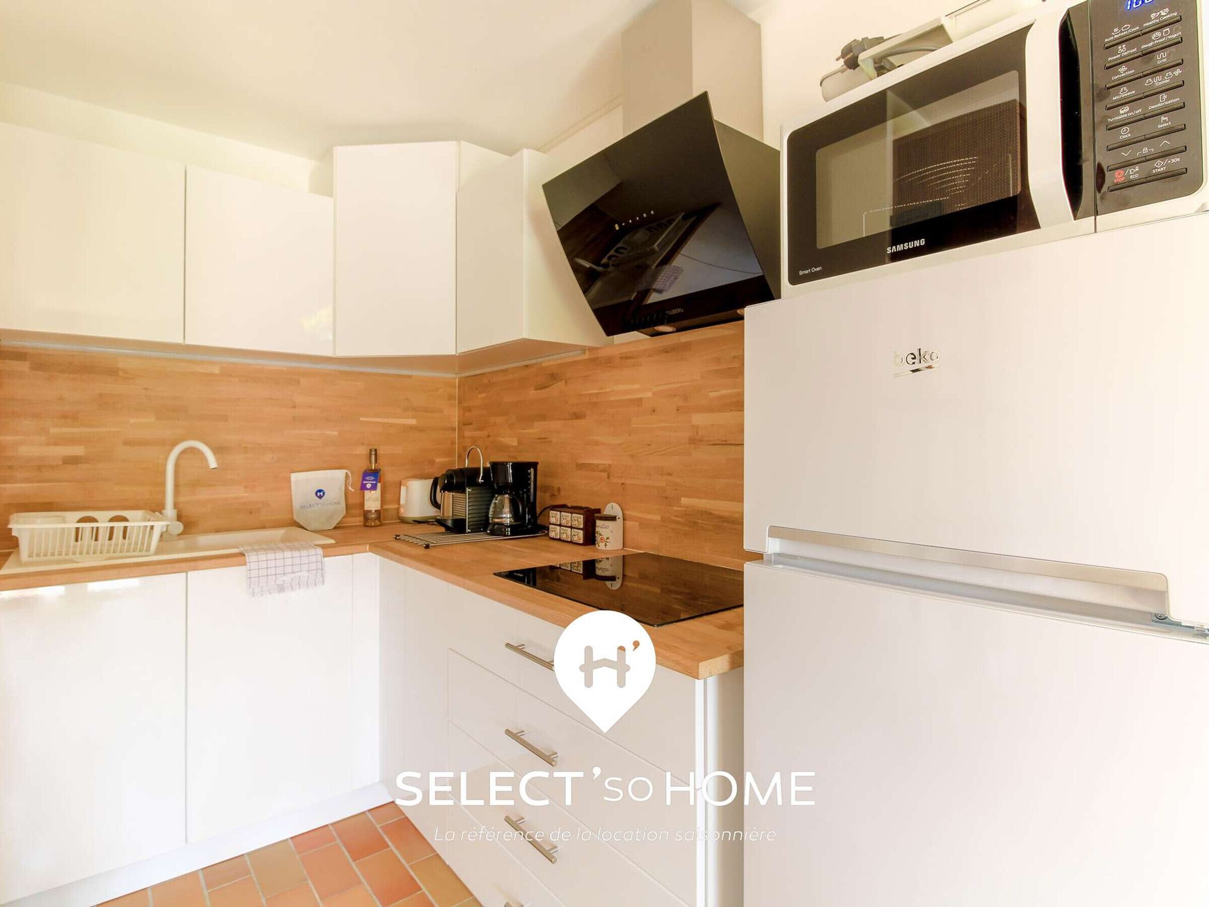 A modern kitchen with white cabinets, a wooden countertop, a built-in microwave, and a refrigerator.