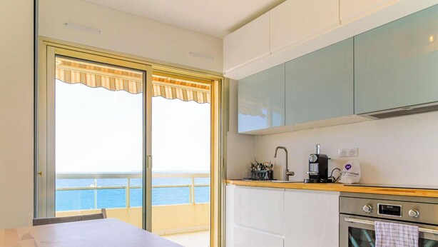 A room with a balcony, a kitchen with a stove, and a view of the sea.