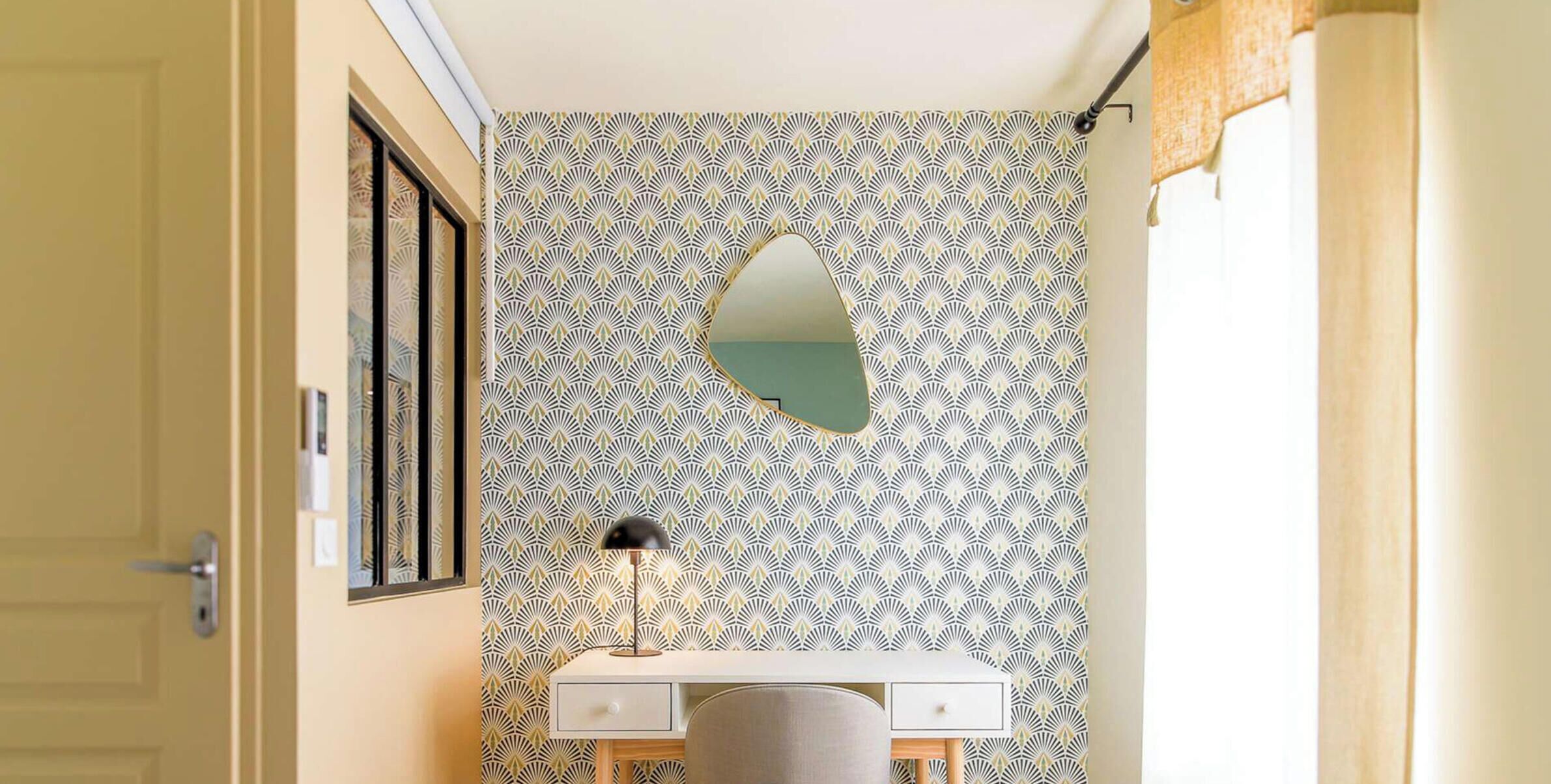 Ein Badezimmer mit ornamentalem Wandpapier, einem Spiegel, einem Schreibtisch und einem Stuhl.