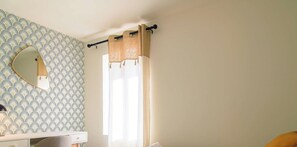 A bathroom with a patterned wallpaper, a mirror, a window with curtains, and a sink.
