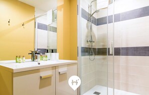 A modern bathroom with a glass-enclosed shower, a white sink with toiletries, and a yellow accent wall.