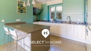 A modern kitchen with a central island, white bar stools, a large window with a view, and pendant lights. - Stunning Villa 8 pers - Jacuzzi - Large Spaces (Le Lavandou)