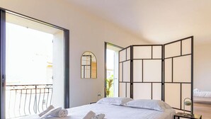 A hotel room with a large bed, a wooden floor, a balcony, and a view of the outside. - Stunning Villa 8 pers - Jacuzzi - Large Spaces (Le Lavandou)