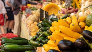 A market stall with various vegetables like zucchini and squash, and a yellow basket.