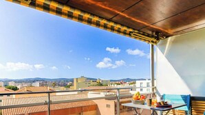 A balcony with a table set for breakfast, overlooking a cityscape with buildings and hills.