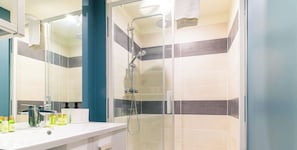 A modern bathroom with a glass shower enclosure, a white vanity with a mirror, and a tiled shower wall.