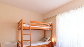 A bunk bed room with a white radiator, a small bedside table with a lamp, and a window with white curtains. - Duplex in Lavandou, Pets Allowed, Parking (Le Lavandou)