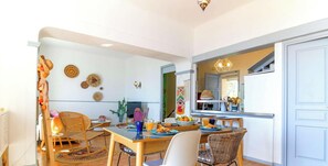 Un comedor con una mesa de madera, sillas de mimbre y vistas a la cocina.