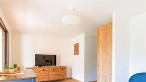 Ein modernes Wohnzimmer mit einem Holz-TV-Schrank, einem blauen Sessel und einem Esstisch mit Stühlen.
