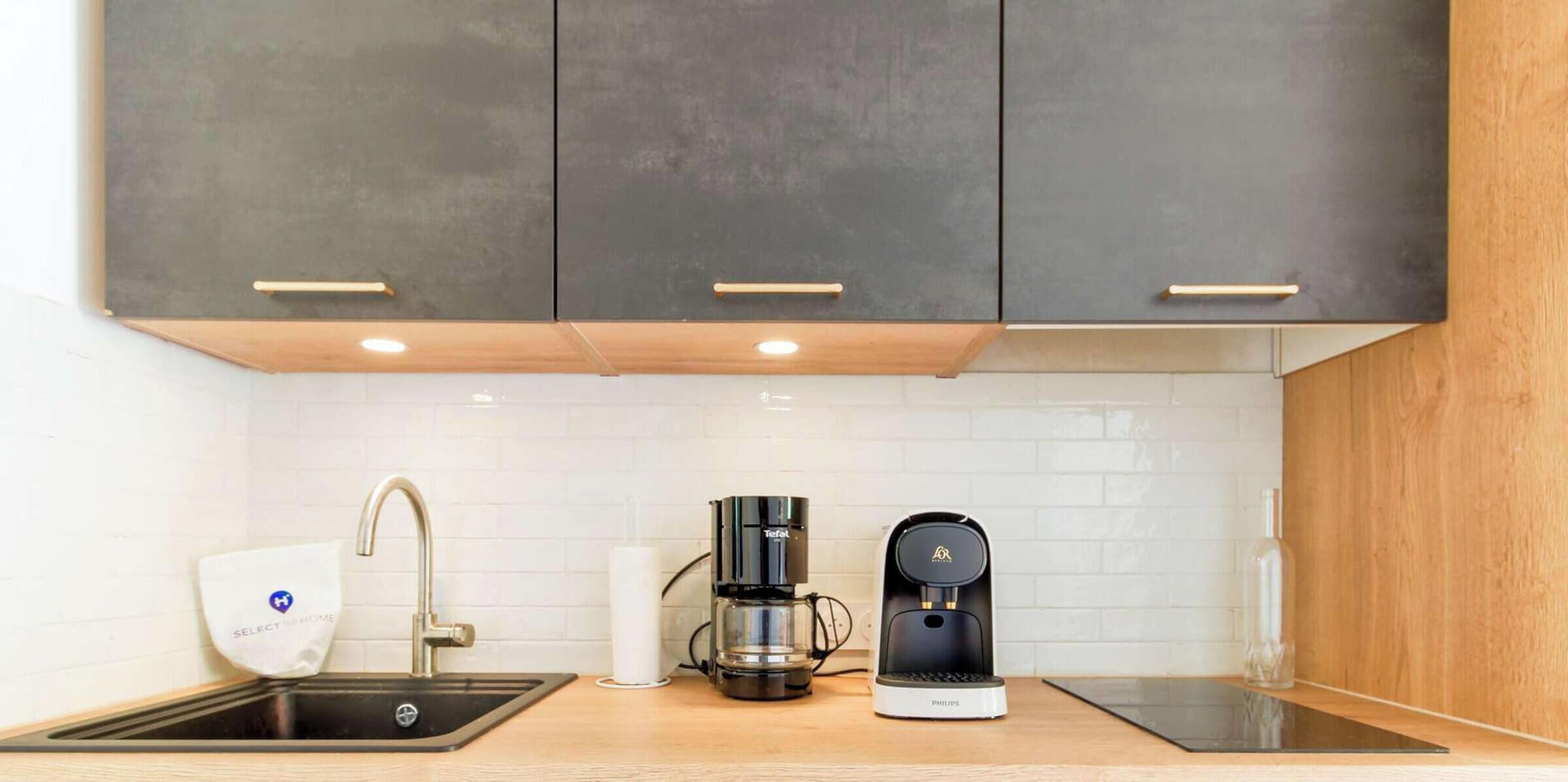 A modern kitchen with a black coffee maker, a white paper towel holder, and a stainless steel sink.