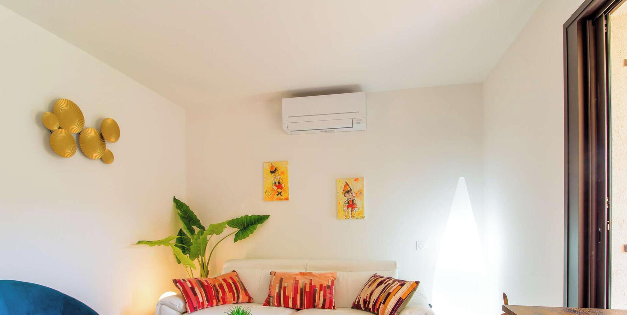 Una sala de estar con un sofá blanco, una planta verde grande y dos aires acondicionados instalados en la pared.