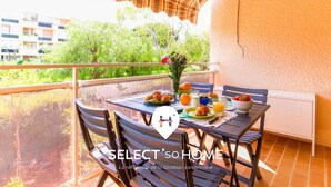 Ein Balkon mit Frühstückstisch, gedeckt mit Croissants, Obst und Saft, mit Blick auf ein Wohngebiet mit Bäumen und Gebäuden.