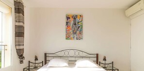 Ein Schlafzimmer mit Bett, zwei Nachttischen, einem Wandbild, einem Fenster mit Vorhängen und einer Klimaanlage.