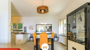 Une cuisine moderne avec un coin repas, comprenant un îlot central, des luminaires suspendus et un meuble vitré contenant des bouteilles de vin.