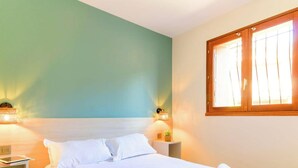 Ein Schlafzimmer mit einem Bett, Nachttischen, Wandlampen und einem Fenster mit Vorhängen.