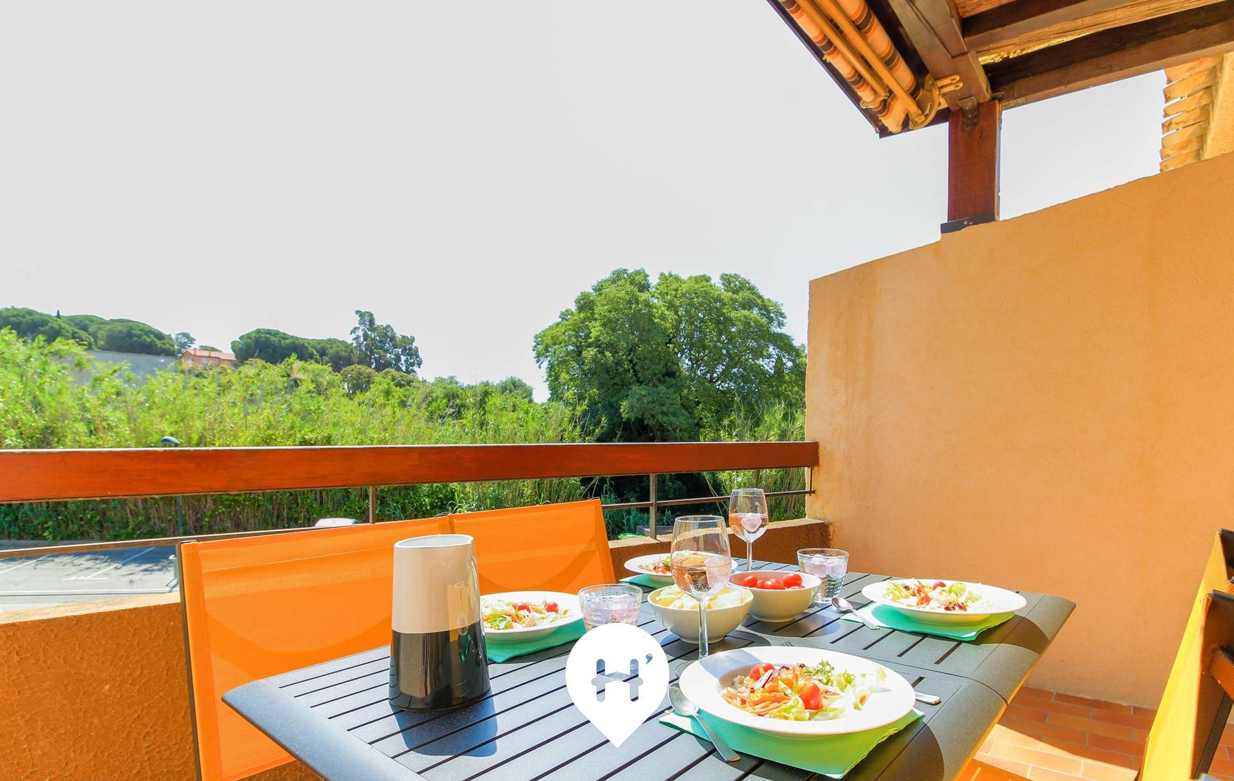 Un espacio de comedor al aire libre con una mesa dispuesta para dos, que incluye platos de comida, vasos y una cafetera.