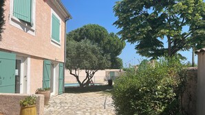 A stone-paved courtyard with a building featuring green shutters and a potted plant. - Detached villa (Marguerittes)