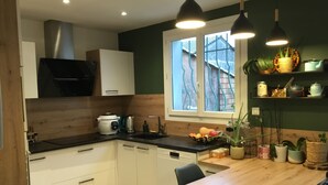 A modern kitchen with white cabinets, a wooden countertop, and a window with a view of a house. There are two pendant lights, a sink, and a stove. - Detached villa (Marguerittes)