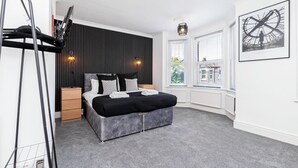 Een moderne slaapkamer met een bed, nachtkastjes, een radiator, een raam met zonwering en een wandklok.