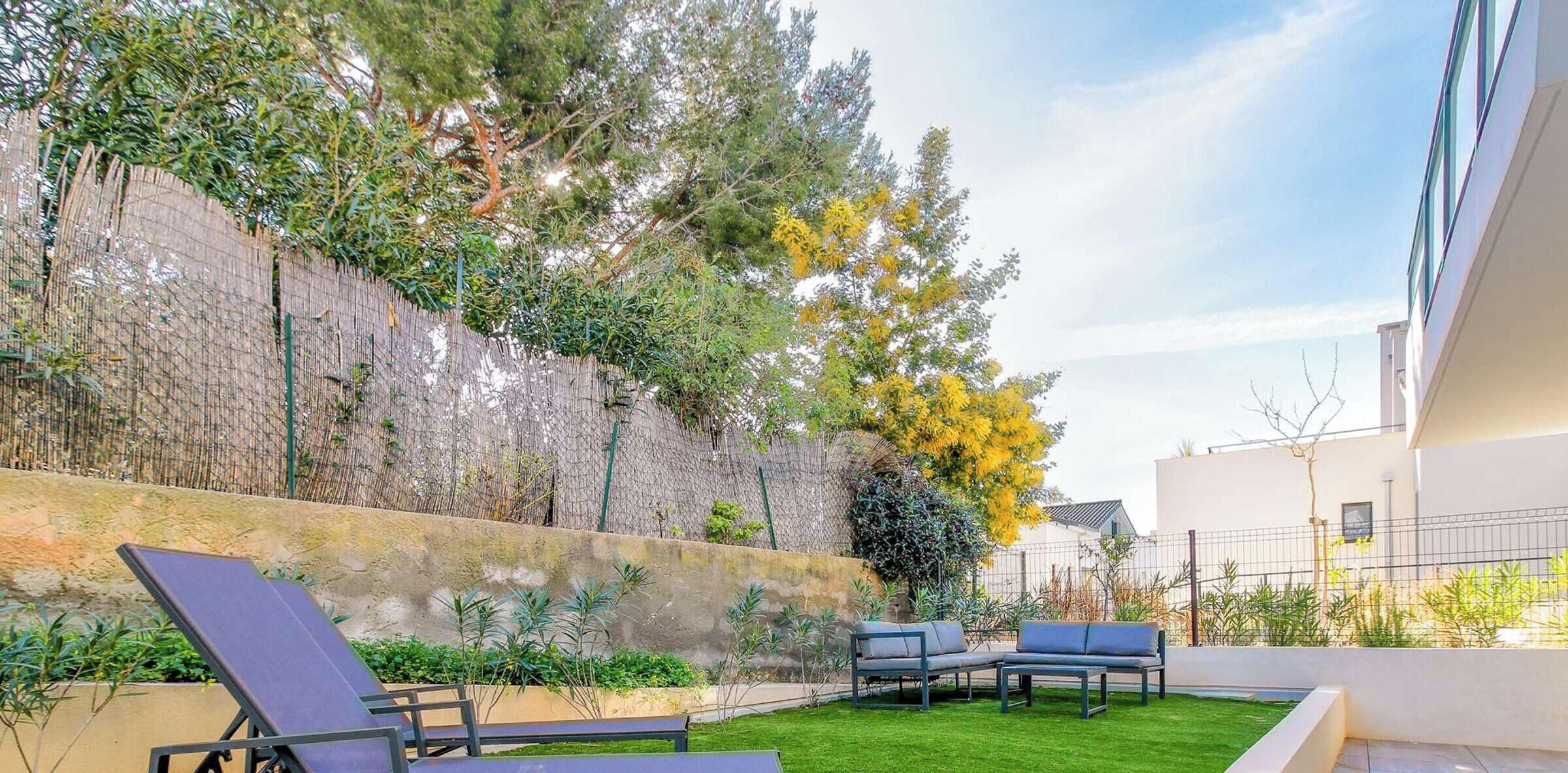 A rooftop garden with two lounge chairs, a small lawn, and a stone wall with climbing plants.