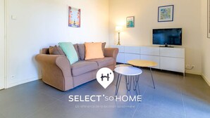 A living room with a sofa, a small round table, a TV on a white cabinet, and a lamp. - Bright loft in Le Lavandou center, pets allowed, 2 bedrooms (Le Lavandou)