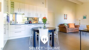 A modern kitchen with white cabinets, a dining area with a round table and chairs, and a living room with a brown sofa and orange cushions. - Bright loft in Le Lavandou center, pets allowed, 2 bedrooms (Le Lavandou)