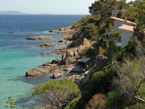 Une propriété située sur la côte, avec un terrain rocheux, un petit bateau et un bâtiment doté d’une terrasse offrant une vue sur la mer.