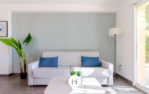 Un salon moderne avec un canapé blanc, deux coussins bleus, une table basse ornée d’une plante et un lampadaire.