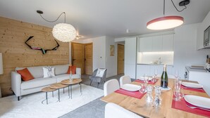 A modern living room with a wooden wall, a sofa, a coffee table, and a dining area with a wooden table set for a meal.
