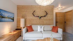 A modern living room with a wooden wall panel, a sofa with cushions, a coffee table, a lamp, and a painting on the wall.