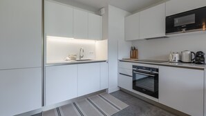 A modern kitchen with white cabinetry, a built-in oven, a microwave, and a coffee maker.