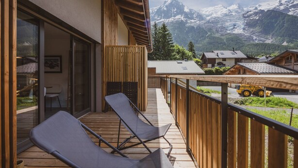 A balcony with two lounge chairs, a wooden railing, and a view of snow-capped mountains.