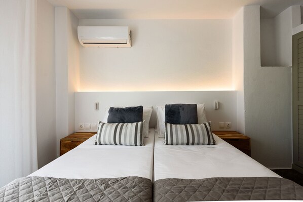 A double bed with a quilted cover, two bedside tables, a wall-mounted air conditioner, and a bedside lamp. - Phaedrus Living: Paros Cycladic Residences 6 (Paros)