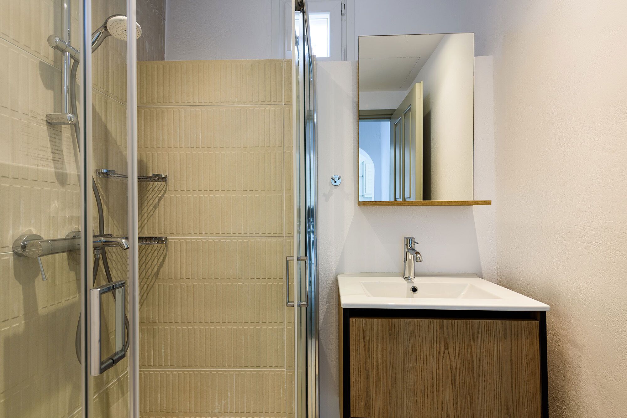 A bathroom with a glass shower enclosure, a wooden vanity, and a mirror above the sink.