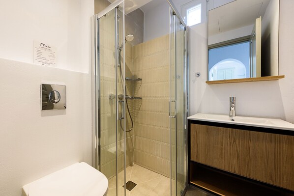 A modern bathroom with a glass-enclosed shower, a white toilet, and a wooden vanity with a mirror.