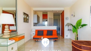 A modern living room with a sofa, a glass coffee table, a lamp, and a plant. - Studio facing the beach - Parking included (Le Lavandou)