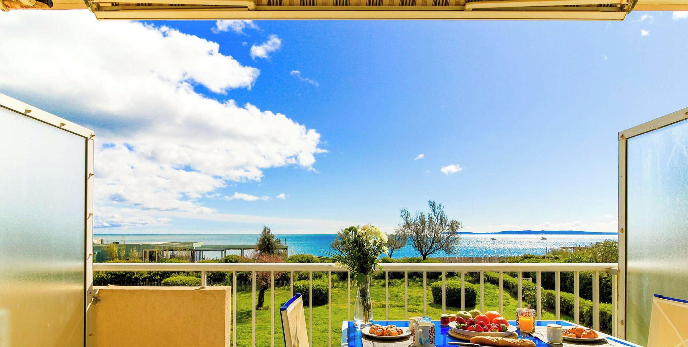 Un balcón con una mesa dispuesta para el desayuno, con vistas a un paisaje marino y tierra a lo lejos.