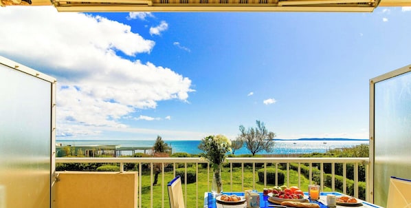 A balcony with a table set for breakfast, overlooking a scenic view of the sea and distant land.
