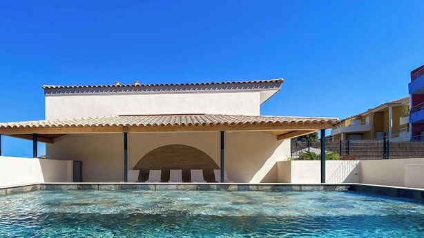 A pool area with a covered seating area and a clear blue sky.