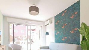 A modern living room with a large window, a flat-screen TV, a sofa, and a decorative wall with a floral pattern.